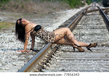 A lovely woman with auburn hair and wearing a tight leopard-print dress, relaxing in the sun on a railroad track.