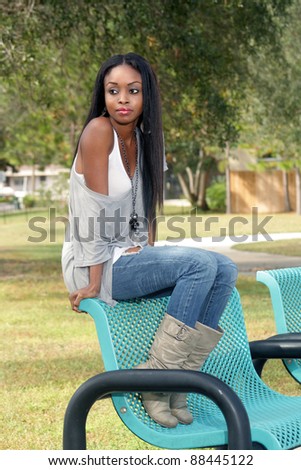 An extraordinarily beautiful young woman sits on a park bench looking off-camera to frame left.