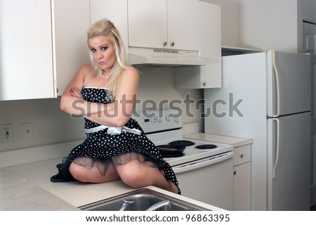 A lovely, glamorous young blonde sits on her kitchen counter.