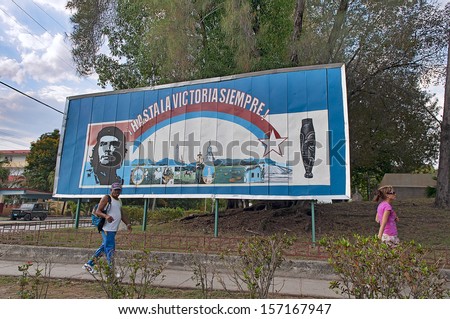 SANTIAGO DE CUBA, CUBA - APRIL 15, 2009. People walking in front of Che Guevara\'s features on a large billboard on the outskirts of Santiago de Cuba, Cuba on April 15, 2009.