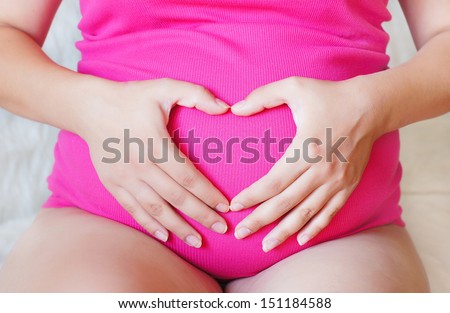 Pregnant hands making a heart on her stomach