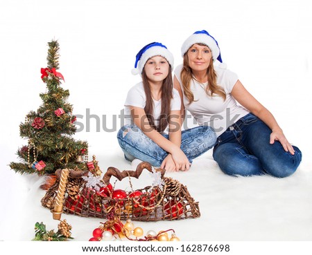 Girl and woman in Santa caps decorating Christmas tree on white background