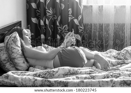 Young Beautiful Woman Lying On Bed And Holding Digital Tablet. Black and white photo