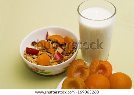 muesli with apples and peaches in a bowl on a napkin with a glass of milk