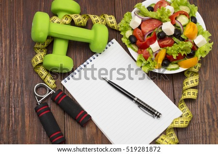 Workout and fitness dieting copy space diary. Healthy lifestyle concept. Dumbbell, vegetable salad and measuring tape on rustic wooden table.