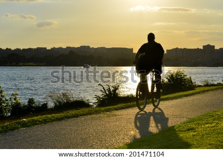 silhouette of a man cyclist riding a road bike on riverside trail