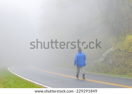 Mysterious man walks into foggy forest road
