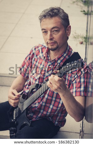Man in short sleeve shirt playing electric guitar in the street
