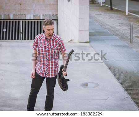 Man in short sleeve shirt holding electric guitar in the street