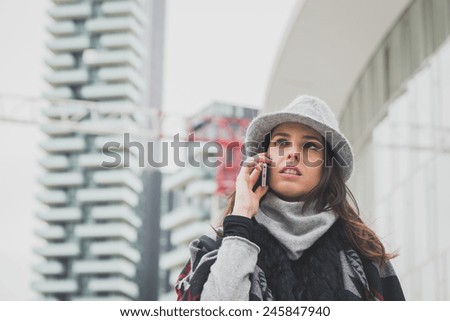 Beautiful young brunette with hat talking on phone in the city streets