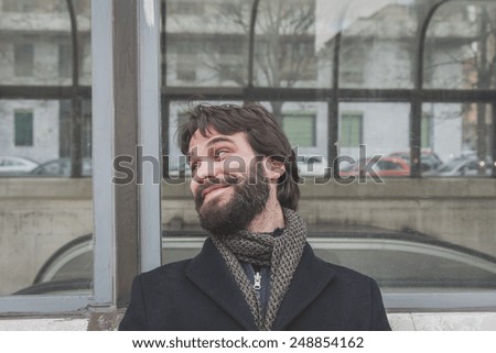 Young handsome bearded man with coat posing in the city streets