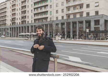 Young handsome bearded man with coat posing in the city streets