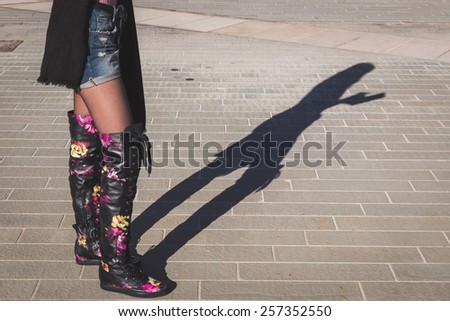 Shadow of a young woman wearing over the knee boots and working on her tablet