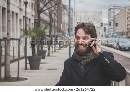 Young handsome bearded man with coat talking on phone in the city streets
