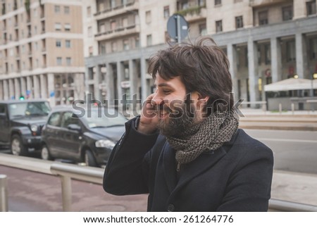 Young handsome bearded man with coat talking on phone in the city streets