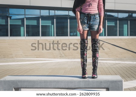 Detail of a beautiful young woman with over the knee boots standing on a bench
