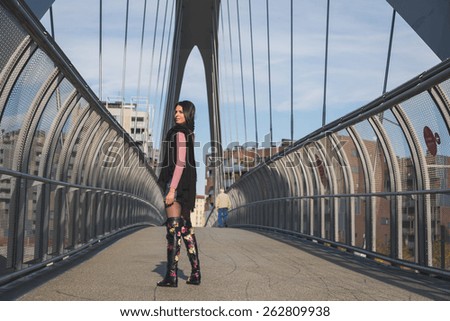 Beautiful young brunette with over the knee boots posing on a bridge