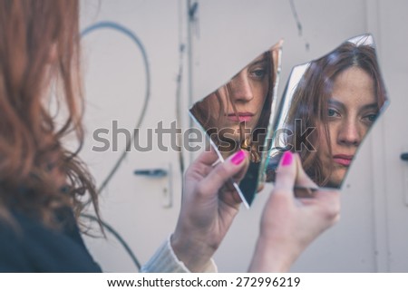 Beautiful redhead girl with long hair and blue eyes looking at herself in a broken mirror