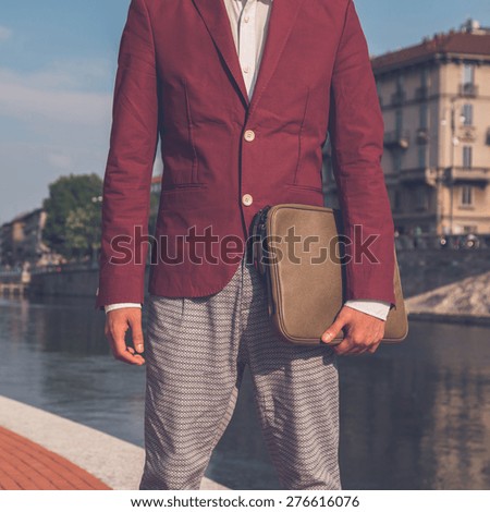 Detail of a young handsome Asian model dressed in red blazer posing by an urban artificial basin