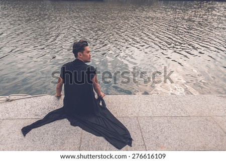 Young handsome Asian model dressed in black tunic sitting by an artificial basin