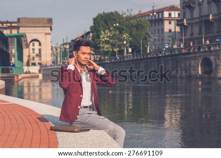 Young handsome Asian model dressed in red blazer sitting by an artificial basin