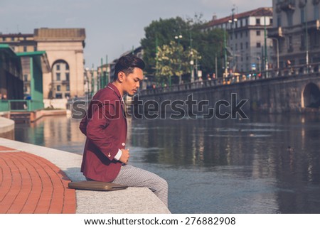 Young handsome Asian model dressed in red blazer sitting by an artificial basin