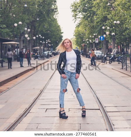 Beautiful blonde girl wearing ripped jeans and leather jacket posing in the city streets