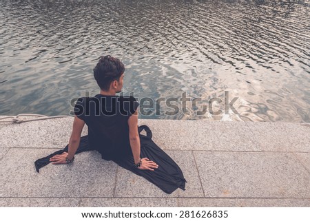 Young handsome Asian model dressed in black tunic sitting by an artificial basin
