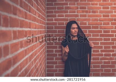 Young handsome Asian model dressed in black tunic posing with a brick wall in background