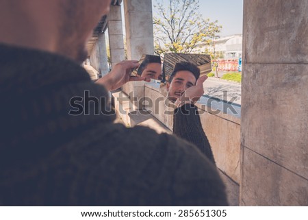 Young handsome man with short hair looking at himself while holding a broken mirror