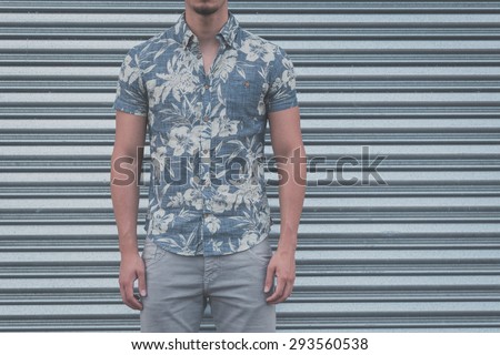 Detail of a young handsome man wearing a short sleeve shirt and posing on a metal backgroung
