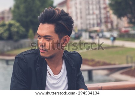 Young handsome Asian model dressed in black posing by an urban artificial basin