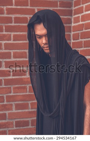 Young handsome Asian model dressed in black tunic posing with a brick wall in background