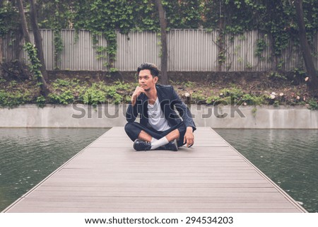 Young handsome Asian model dressed in black posing by an urban artificial basin