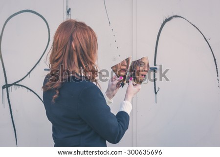 Beautiful redhead girl with long hair and blue eyes looking at herself in a broken mirror