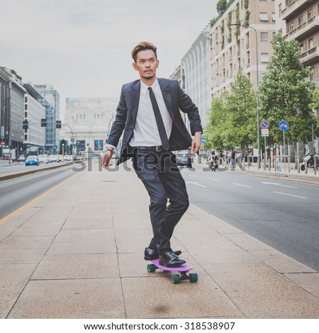 Young handsome Asian model dressed in dark suit and tie riding his skateboard