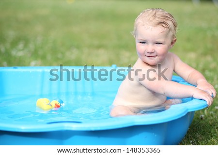 Cute happy baby playing in plastic kiddie pool in the backyard