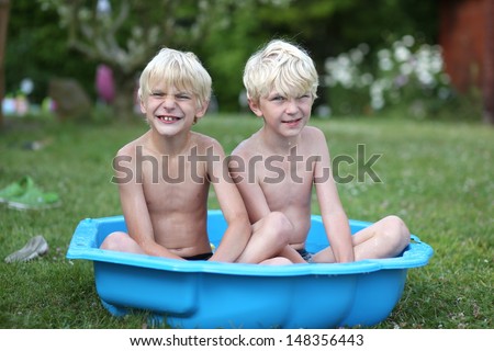 Two funny twin brothers sitting in a small plastic kiddie pool at the backyard of the house