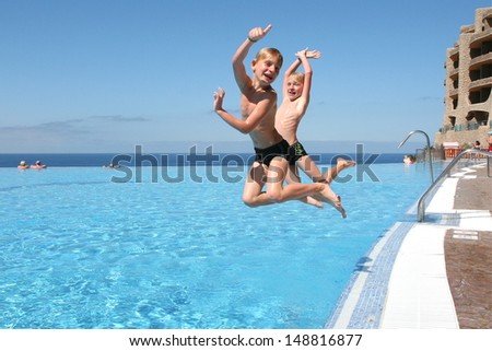 Two happy twin brothers are jumping into infinity swimming pool at the resort with ocean at the background