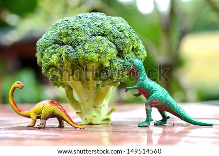 Funny Picture Of Toy Dinosaur Eating Broccoli Tree. Photo Can Be Used To Help Cooking With Children, Preparing Kid-Friendly Dishes And Promoting Healthy Food For Children