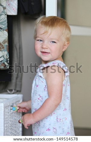 Funny baby girl is playing with white storage basket in a white wardrobe