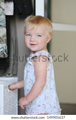 Lovely baby girl plays with white storage basket in a big wardrobe