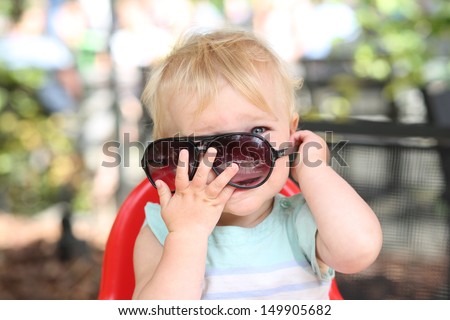 Cute happy baby girl playing peek a boo behind big sunglasses