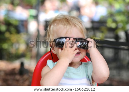 Lovely happy baby girl playing peek a boo behind big sunglasses
