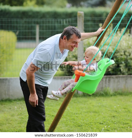 Happy father with his adorable baby daughter playing with swing in the garden at backyard of the house