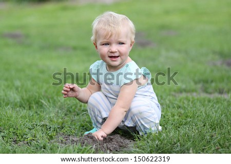 Adorable baby girl sitting in a grass in the middle of a big farm playing with mud