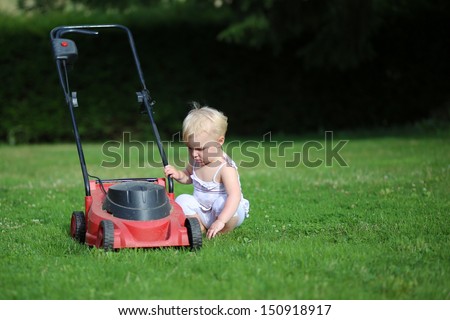 Curious little baby girl is playing outside, trying to investigation how lawn machine works