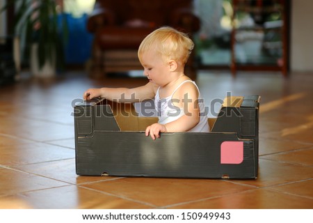 Cute Creative Blond Little Baby Girl Plays With Cardboard Box Sitting Inside Of It