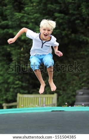 Happy boy plays outdoors in garden jumping high in the sky on trampoline