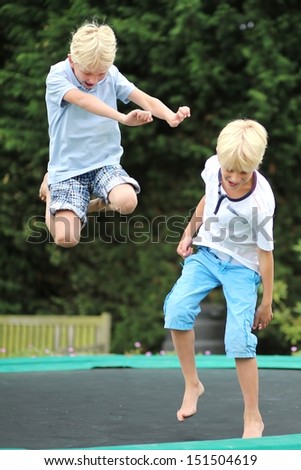 Two happy boys, twin brothers, are playing outdoors in a garden jumping high in the sky on trampoline
